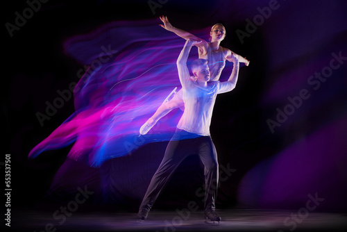 Support. Portrait of young man and woman, figure skating athletes dancing isolated over black background in neon with mixed lights