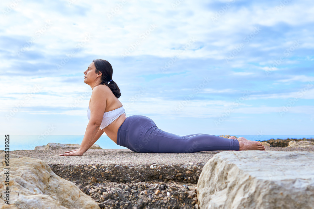 middle aged latin woman practicing yoga and mindfulness on the rocky pier by the sea