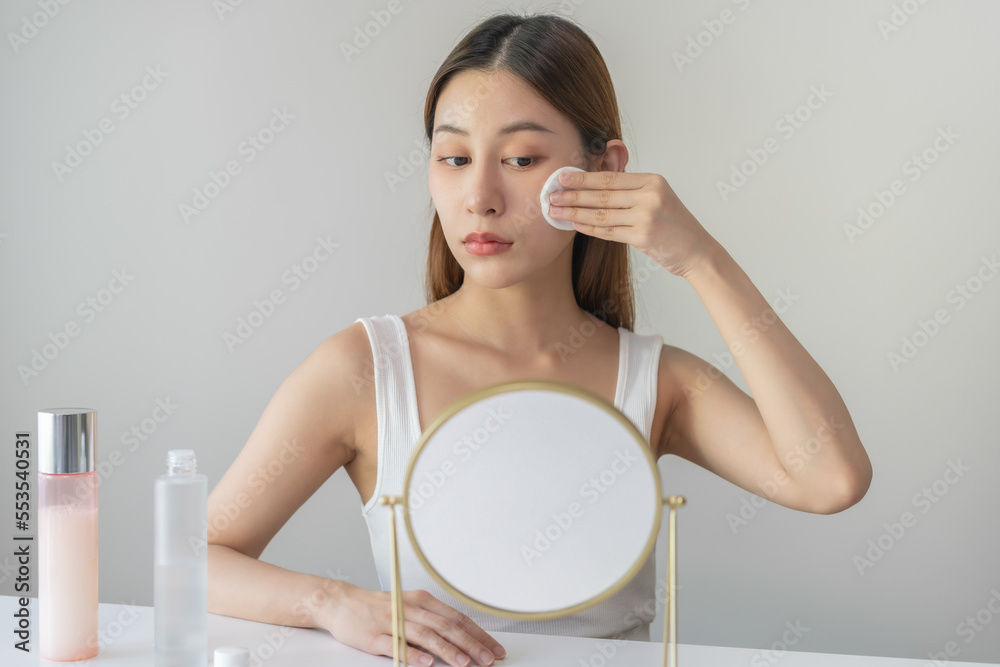 Happy beauty, attractive asian young woman, girl looking reflect in mirror, hand holding cotton pad, applying facial wipe on her face remover makeup, essence or lotion for treatment, skin care routine Happy beauty, attractive asian young woman, girl looking reflect in mirror, hand holding cotton pad, applying facial wipe on her face remover makeup, essence or lotion for treatment, skin care routine