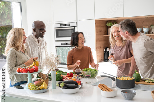 Group of diverse middle-aged friends getting together for dinner chatting in kitchen while cooking