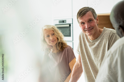 Portrait of middle-aged couple chatting with friends in kitchen