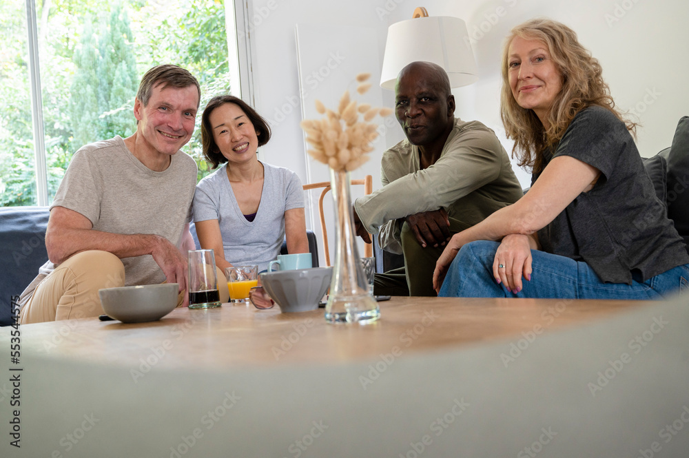 Portrait of diverse group of senior friends enjoying themselves at home and looking at camera
