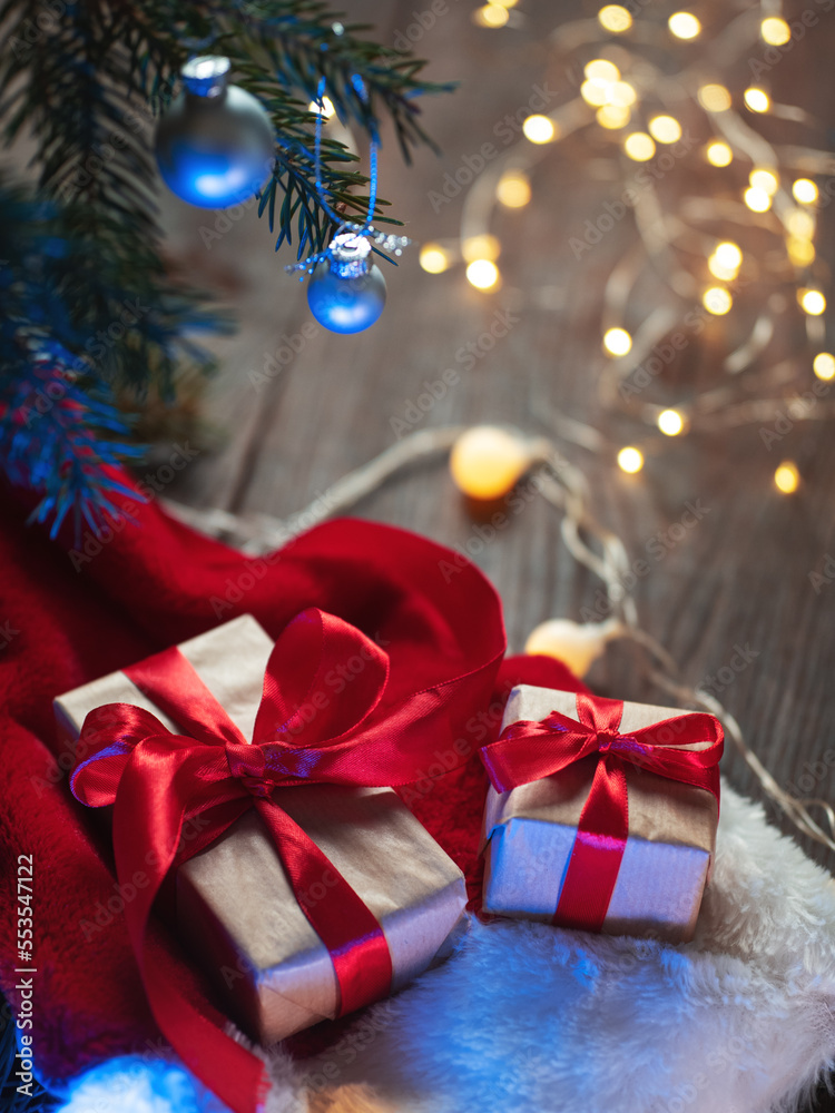 Christmas Gift boxes with red ribbons packed in kraft paper under the Christmas tree. Santa hat and garland , wooden table Christmas Gift boxes with red ribbons packed in kraft paper under the Christmas tree. Santa hat and garland , wooden table