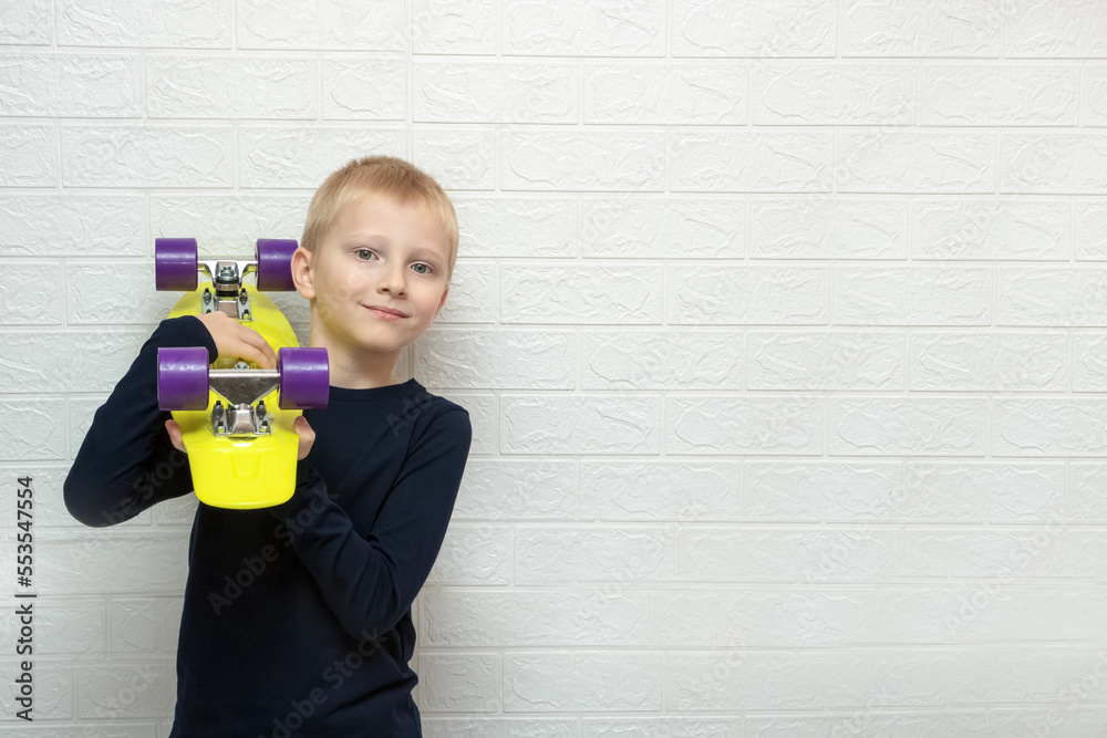 boy holds a skateboard on his shoulder against the background of a wall with copy space, passion, free time boy holds a skateboard on his shoulder against the background of a wall with copy space, passion, free time