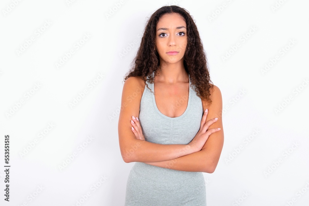 Serious pensive teen girl with curly hair wearing grey sport set over white background feel like cool confident entrepreneur cross hands. Serious pensive teen girl with curly hair wearing grey sport set over white background feel like cool confident entrepreneur cross hands.