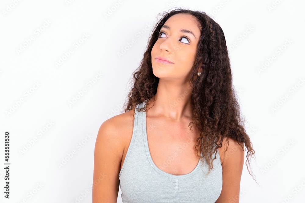 teen girl with curly hair wearing grey sport set over white background looking aside into empty space thoughtful teen girl with curly hair wearing grey sport set over white background looking aside into empty space thoughtful
