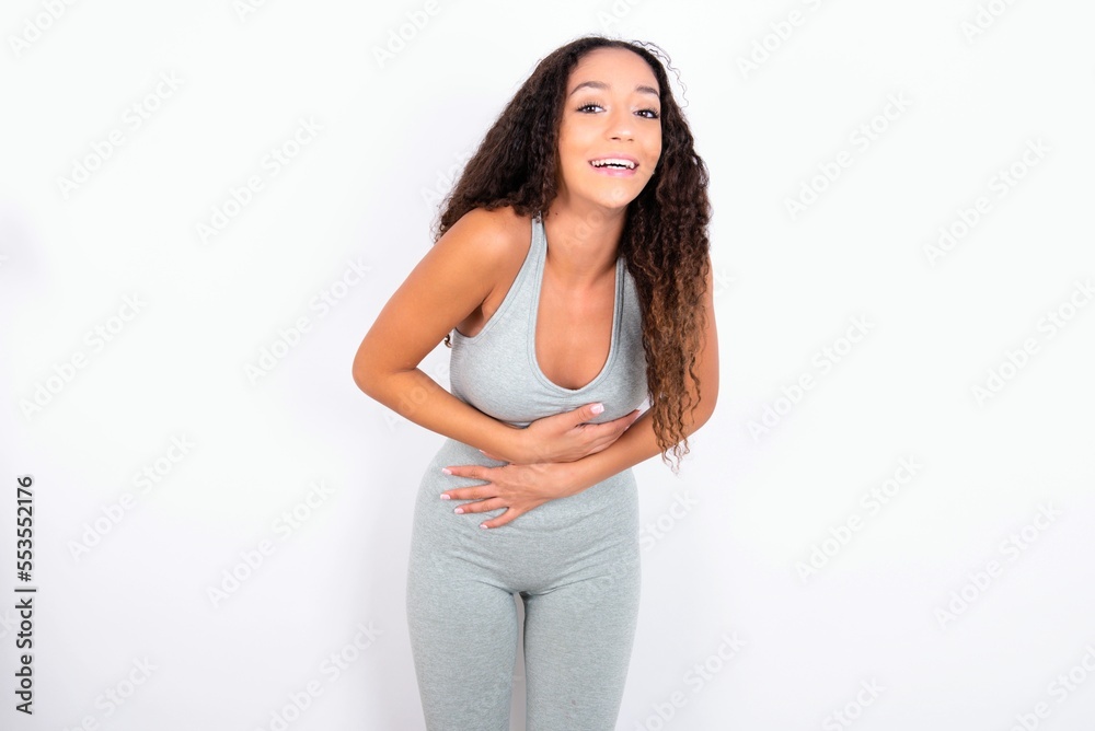 teen girl with curly hair wearing white sport set over gray background smiling and laughing hard out loud because funny crazy joke with hands on body. teen girl with curly hair wearing white sport set over gray background smiling and laughing hard out loud because funny crazy joke with hands on body.