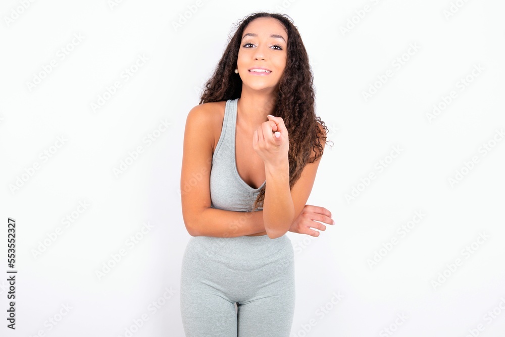 teen girl with curly hair wearing white sport set over gray background Beckoning come here gesture with hand inviting welcoming happy and smiling teen girl with curly hair wearing white sport set over gray background Beckoning come here gesture with hand inviting welcoming happy and smiling