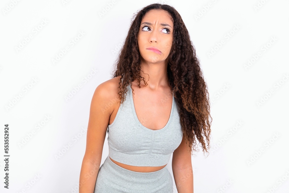 Beautiful teen girl with curly hair wearing grey sport set over white background making grimace and crazy face, screaming out of control, funny lunatic expressing freedom and wild. Beautiful teen girl with curly hair wearing grey sport set over white background making grimace and crazy face, screaming out of control, funny lunatic expressing freedom and wild.