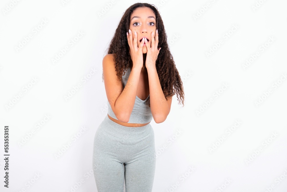 Scared terrified Beautiful teen girl with curly hair wearing green sport set over white background shocked with prices at shop, People and human emotions concept Scared terrified Beautiful teen girl with curly hair wearing green sport set over white background shocked with prices at shop, People and human emotions concept