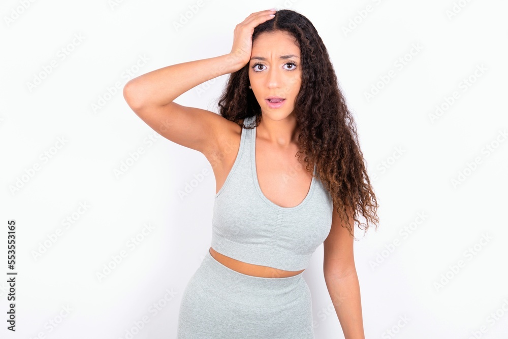 Embarrassed Beautiful teen girl with curly hair wearing green sport set over white background with shocked expression, expresses great amazement, Puzzled model poses indoor Embarrassed Beautiful teen girl with curly hair wearing green sport set over white background with shocked expression, expresses great amazement, Puzzled model poses indoor