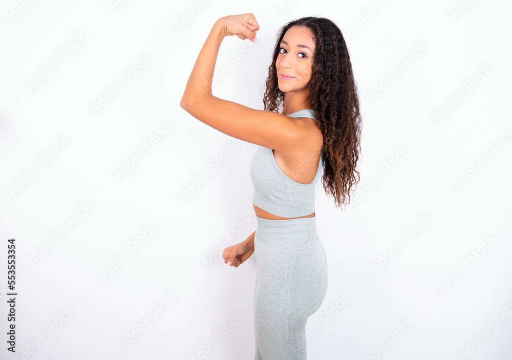 Portrait of powerful cheerful Beautiful teen girl with curly hair wearing green sport set over white background showing muscles. Portrait of powerful cheerful Beautiful teen girl with curly hair wearing green sport set over white background showing muscles.