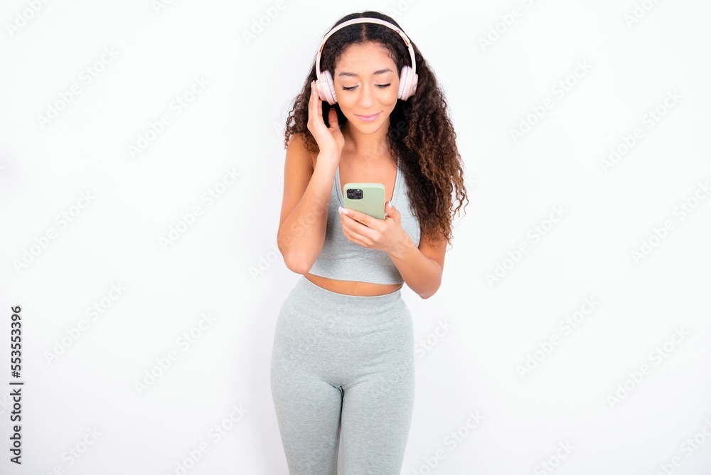 Happy Beautiful teen girl with curly hair wearing green sport set over white background feels good while focused in screen of smartphone. People, technology, lifestyle Happy Beautiful teen girl with curly hair wearing green sport set over white background feels good while focused in screen of smartphone. People, technology, lifestyle