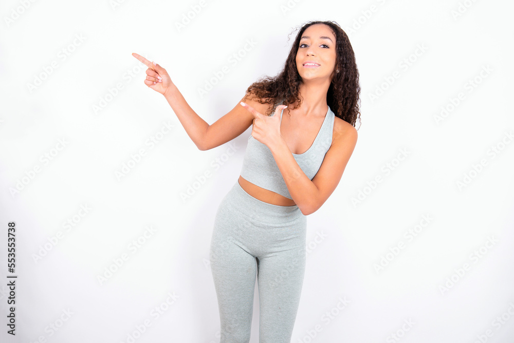 Beautiful teen girl with curly hair wearing green sport set over white background point at copyspace recommend sales discounts Beautiful teen girl with curly hair wearing green sport set over white background point at copyspace recommend sales discounts