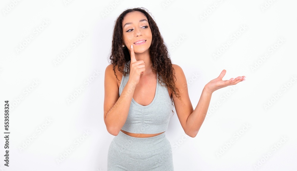 Funny teen girl with curly hair wearing white sport set over gray background holding open palm new product. I wanna buy it! Funny teen girl with curly hair wearing white sport set over gray background holding open palm new product. I wanna buy it!