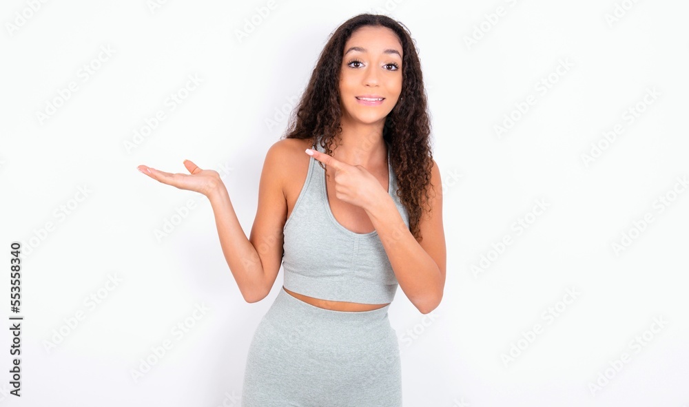 teen girl with curly hair wearing white sport set over gray background pointing and holding hand showing adverts teen girl with curly hair wearing white sport set over gray background pointing and holding hand showing adverts