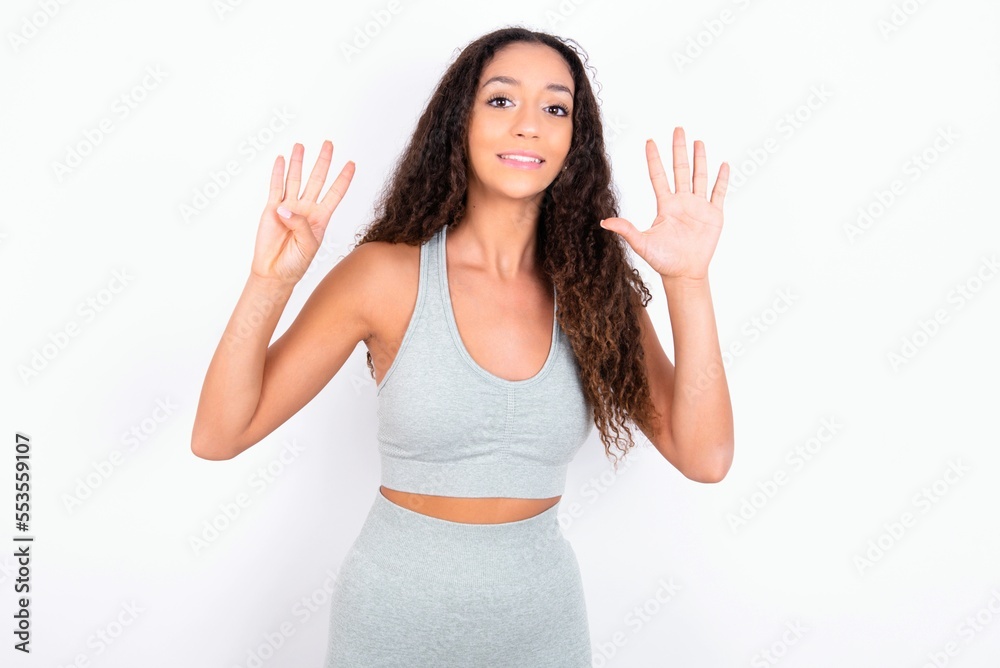 teen girl with curly hair wearing white sport set over gray background showing and pointing up with fingers number nine while smiling confident and happy.
