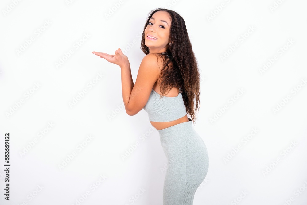 teen girl with curly hair wearing white sport set over gray background pointing aside with hands open palms showing copy space, presenting advertisement smiling excited happy teen girl with curly hair wearing white sport set over gray background pointing aside with hands open palms showing copy space, presenting advertisement smiling excited happy