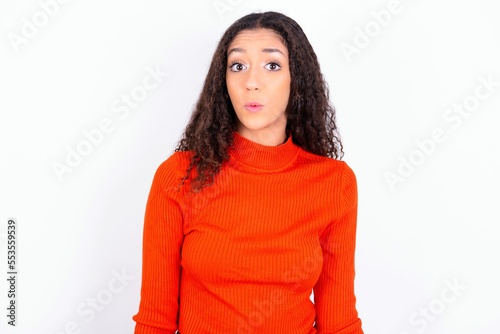 teen girl wearing knitted red sweater over white background expressing disgust, unwillingness, disregard having tensive look frowning face, looking indignant with something. © Jihan