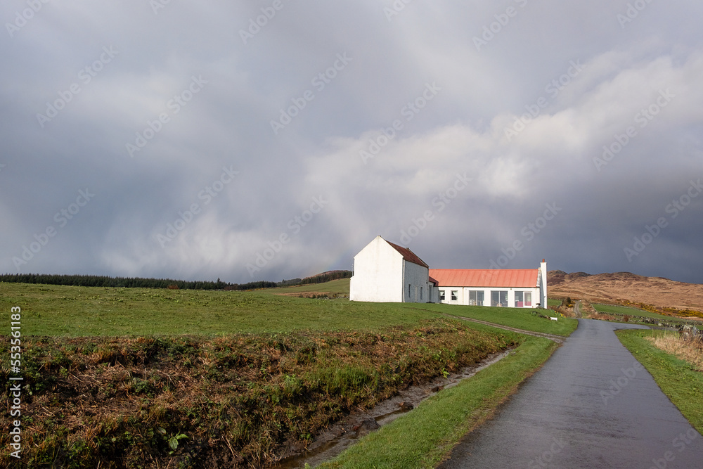 Lonely farmhouse with red pantiles roof surrounded by green pastures, against a dramatic cloudy sky, beautiful solitary landscape common to Scottish Highlands,  Kilberry, Scotland, UK