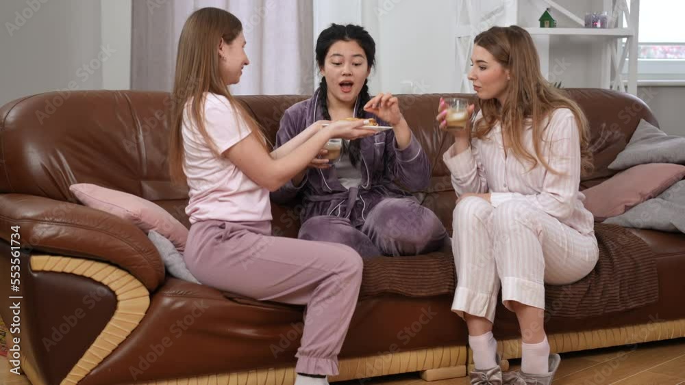 Wide shot relaxed Asian and Caucasian women with cappuccino sitting on couch as friend entering living room with crepes. Young beautiful ladies tasting unsavory dessert with bad taste Wide shot relaxed Asian and Caucasian women with cappuccino sitting on couch as friend entering living room with crepes. Young beautiful ladies tasting unsavory dessert with bad taste