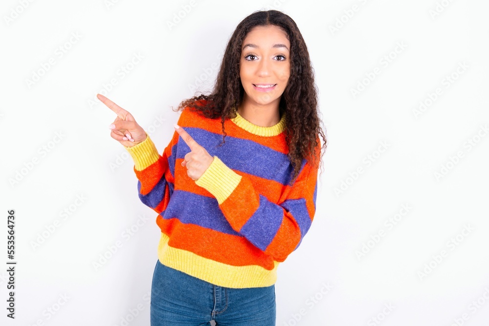 beautiful teen girl wearing knitted colourful sweater over white background points at copy space indicates for advertising gives right direction beautiful teen girl wearing knitted colourful sweater over white background points at copy space indicates for advertising gives right direction