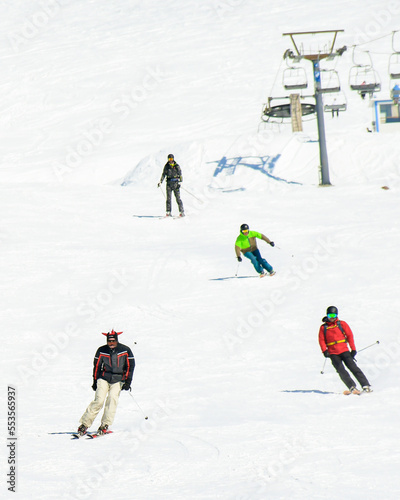 Four friends skiers boarders front view ski downhill on holiday in ski resort have fun together in mountains