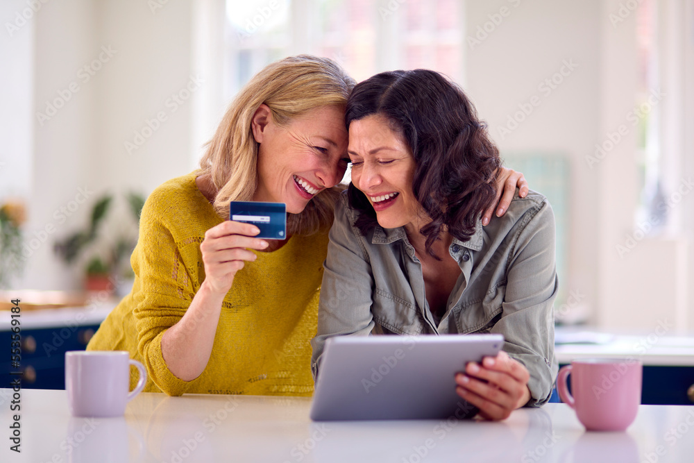 Same Sex Mature Female Couple With Credit Card Using Digital Tablet At Home To Book Holiday Or Shop