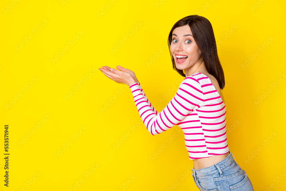 Photo portrait of gorgeous young woman excited palms hold product empty space wear stylish striped look isolated on yellow color background Photo portrait of gorgeous young woman excited palms hold product empty space wear stylish striped look isolated on yellow color background