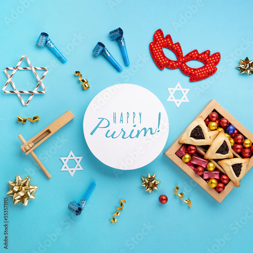 Purim homemade hamantaschen cookies, red carnival mask, noisemaker, sweet candies and party decor on blue background. photo