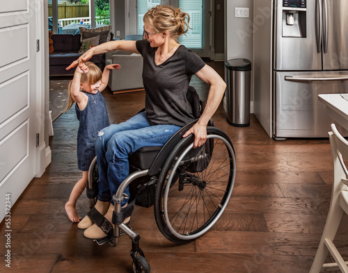 A paraplegic mother dancing with her daughter in the kitchen using her whellchair: Edmonton, Alberta, Canada photo