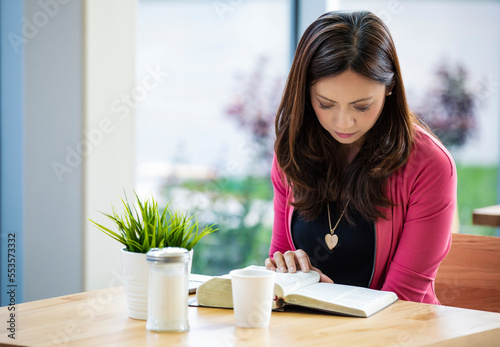 A mature Asian Christian woman studying her bible near a window in a coffee shop: Edmonton, Alberta, Canada
