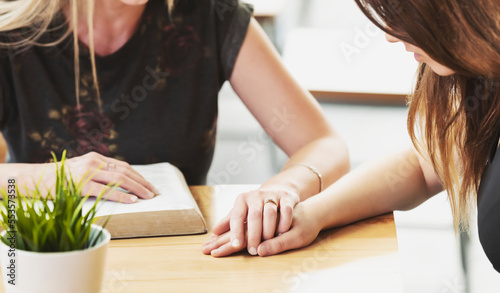 A mature Christian woman mentoring and praying with a young woman during a bible study in a coffee shop at a church: Edmonton, Alberta, Canada