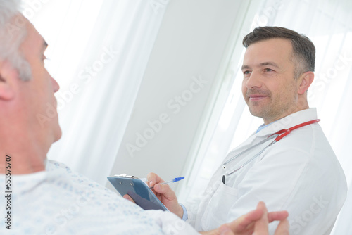 male doctor writing medical report of senior man on clipboard