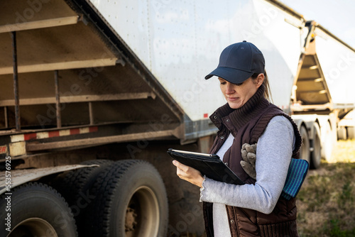 Mature woman working on her farm, holding a tablet computer and standing next to the flatbed of a grain truck; Alcomdale, Alberta, Canada