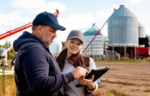 Mature couple working on their farm, standing in front of their grainery while consulting tablet computer; Alcomdale, Alberta, Canada photo