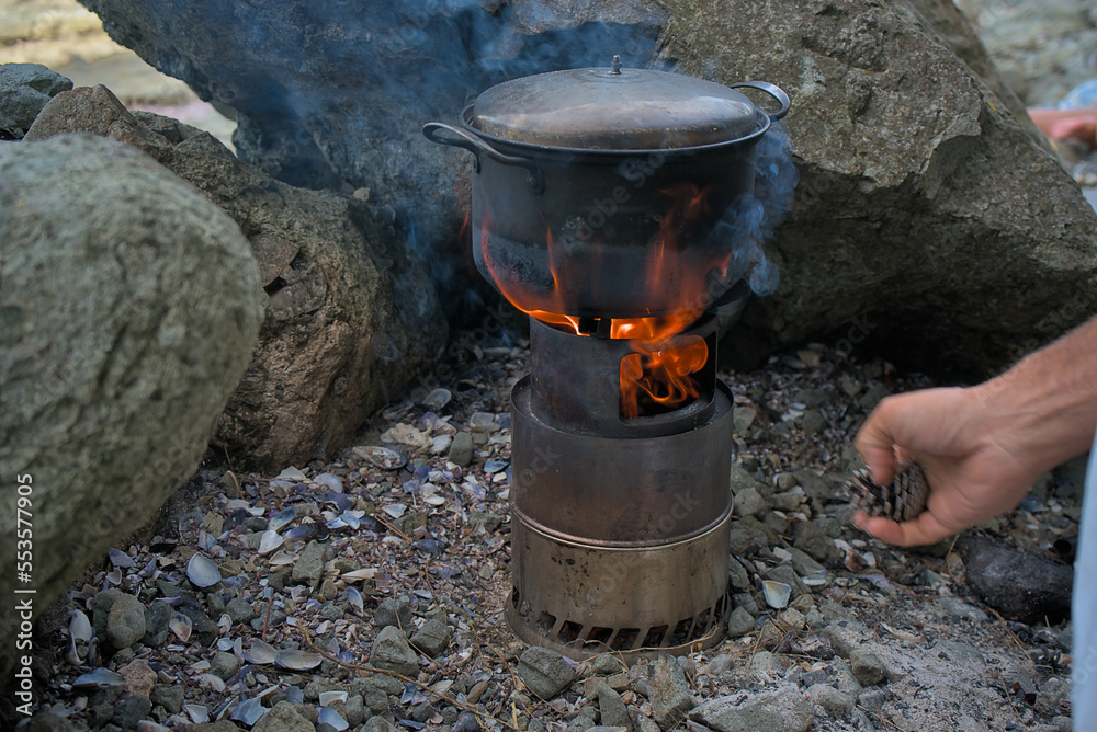 Wood burner for cooking outdoors in the wild. Surrounded by stones, food is cooked in a pot on a safe fire. tourist vacation Wood burner for cooking outdoors in the wild. Surrounded by stones, food is cooked in a pot on a safe fire. tourist vacation