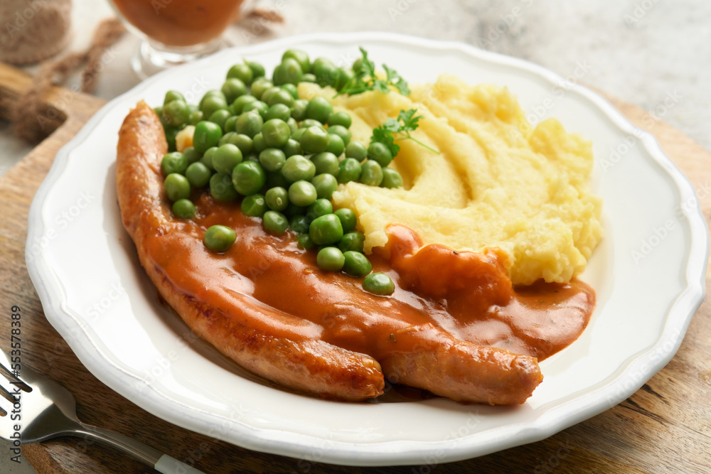 Bangers and mash. Grilled sausages with mash potato and green pea on white plate on grey background. Traditional dish of Great Britain and Ireland. BBQ beef sausages. Top view.