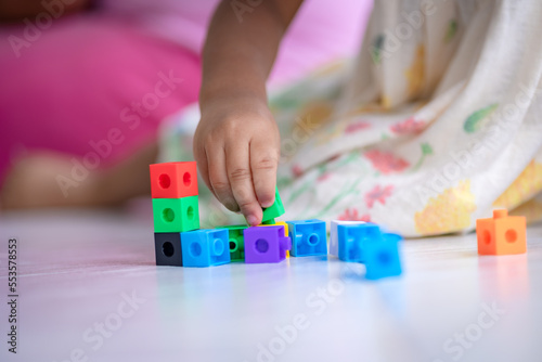 Girl is using hands assembling colored cubes in child development builder concept.
