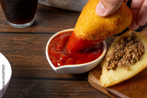 dipping coxinha on the ketchup sauce. traditional brazilian fried coxinha snack fast food photo