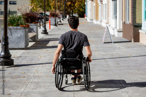 Young paraplegic man in his wheelchair going down a city walkway on a beautiful fall day; Edmonton, Alberta, Canada photo