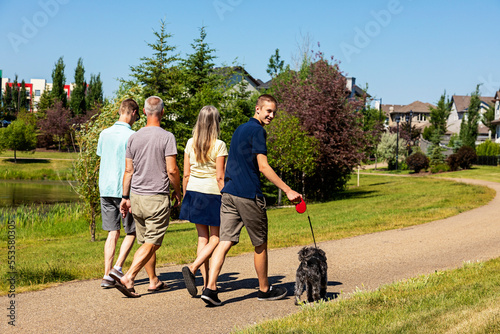Family with two teenage sons walk together in a neighbourhood park with their dog on a beautiful sunny day; Edmonton, Alberta, Canada