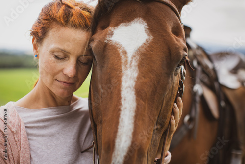Фотография Pretty, young, redhead woman with her lovely horse, during her favorite leisure