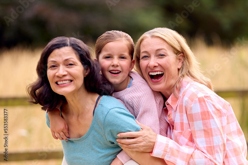 Portrait Of Same Sex Family With Two Loving Mature Mums Hugging Daughter On Walk In Countryside