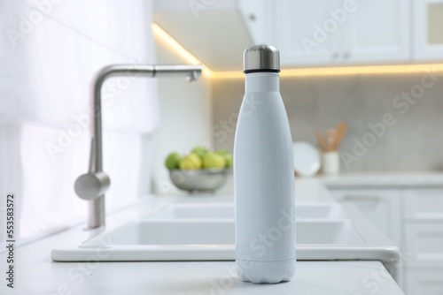 Stylish thermo bottle on white countertop in kitchen. Space for text