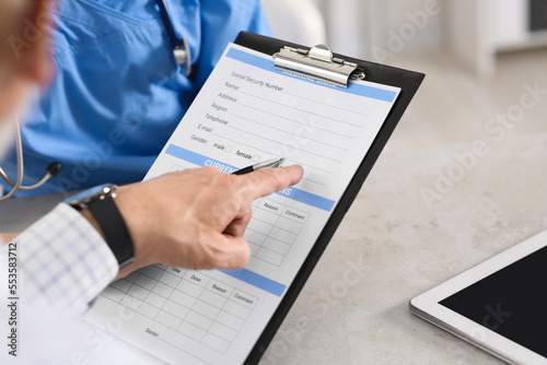 Doctor showing medical card to patient at table in clinic, closeup