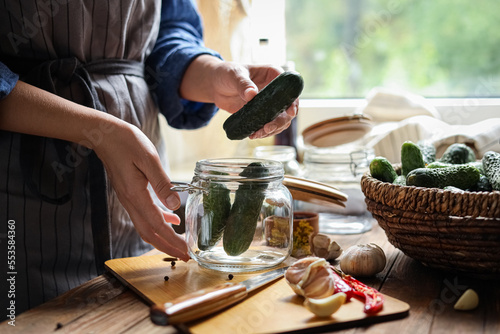 Woman putting cucumbers into jar at wooden table, closeup. Pickling vegetables