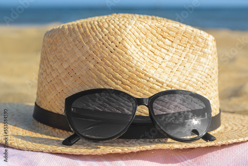 Hat with beautiful sunglasses on blanket near sea, closeup