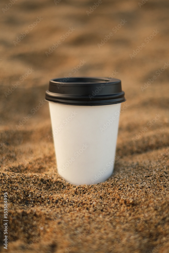 mockup of a disposable white cup of coffee to go on the beach close-up mockup of a disposable white cup of coffee to go on the beach close-up