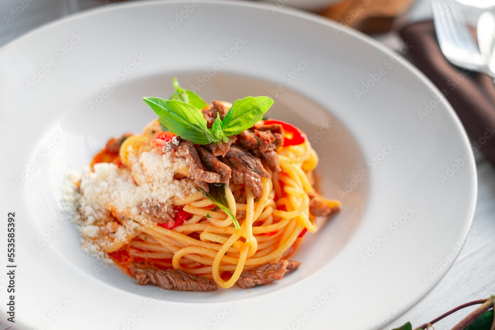Spaghetti pasta with tomato sauce and beef stew, tomatoes, parmesan cheese and fresh basil on a wooden background. Italian cuisine Spaghetti pasta with tomato sauce and beef stew, tomatoes, parmesan cheese and fresh basil on a wooden background. Italian cuisine